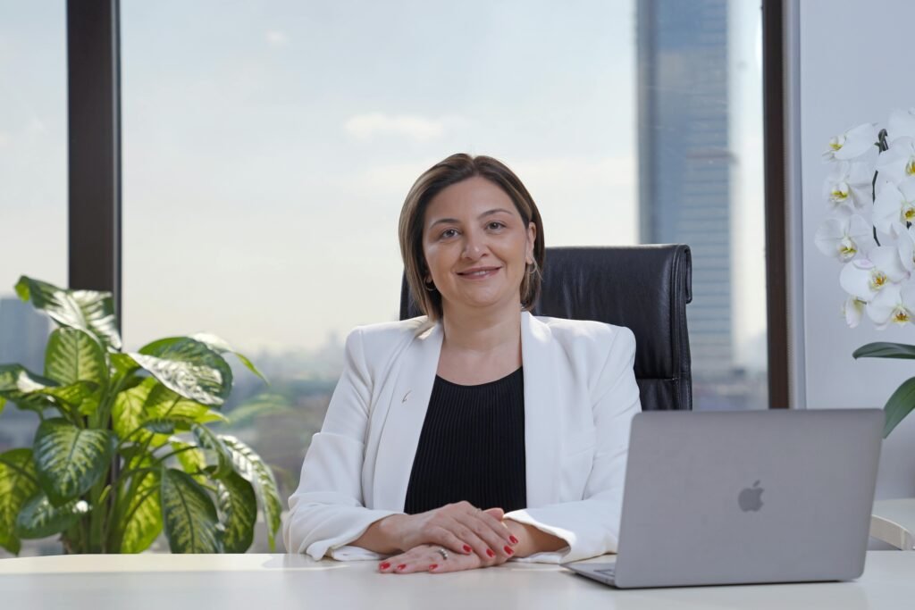 Professional woman in a white suit sitting confidently at a desk with a laptop in a modern office.
